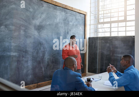 Konzentriert und selbstbewusst jungen afrikanischen Geschäftsfrau, im Gespräch mit Kollegen und hält einen Vortrag auf einer Tafel in einem modernen Büro Stockfoto
