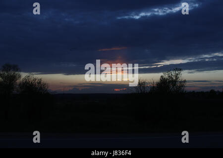 Feurige Strahlen der Sonne am Himmel mit bunten Wolken bei Sonnenuntergang. Stockfoto