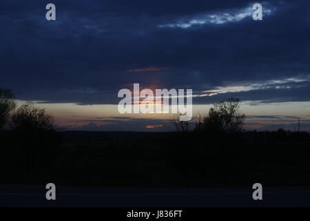 Feurige Strahlen der Sonne am Himmel mit bunten Wolken bei Sonnenuntergang. Stockfoto