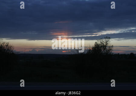 Feurige Strahlen der Sonne am Himmel mit bunten Wolken bei Sonnenuntergang. Stockfoto