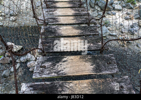 Altmodisches hölzernen Sprossen einer Kabel- und Zaun Draht-Hängebrücke über einen kleinen Fluss im nördlichen Insel Luzon, Philippinen. Stockfoto