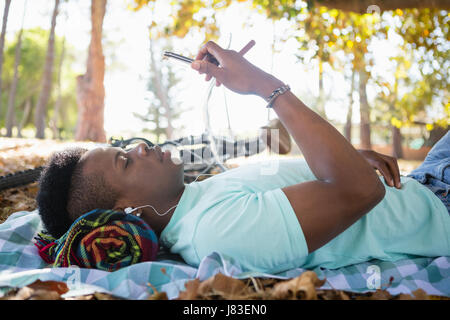 Junger Mann mit Handy liegend auf einer Picknickdecke Stockfoto