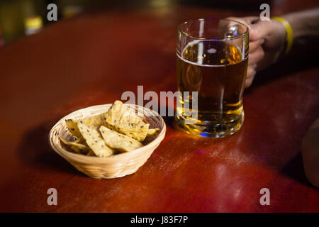 Nahaufnahme von mans Hand mit einem Krug Bier mit Imbiss am Tresen Stockfoto