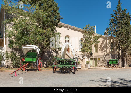 Eine historische Ochsenwagen und zwei Pferde oder Ochsen gezogenen Karren vor das historische Bahnhofsgebäude in Matjiesfontein, heute ein museum Stockfoto