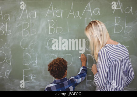 Lehrer, die Schüler schriftlich Alphabet auf Tafel in der Schule zu unterstützen Stockfoto