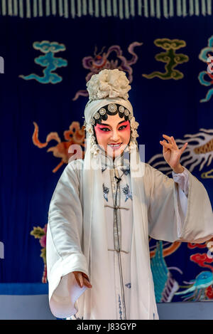 Eine weibliche Darstellerin der Peking-Oper oder Kunqu-Oper in weiß gekleidet, vor bunten Teppich im Cangpo Ancient Village, Boteli County, China führt. Stockfoto