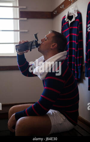Müde Rugby-Spieler Trinkwasser sitzend auf Bank gegen die Wand Stockfoto