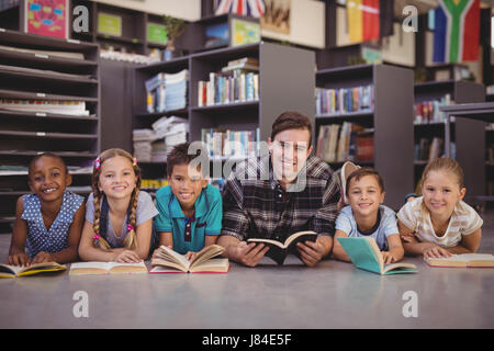Porträt von Lehrer und Schüler auf Boden beim Lesen Bücher in der Bibliothek in der Schule Stockfoto