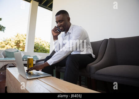 Lächelnde Geschäftsmann mit Laptop während des Gesprächs am Telefon Stockfoto
