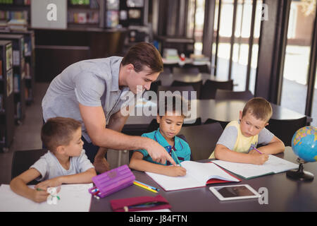 Lehrer, die Schüler bei den Hausaufgaben in der Bibliothek in der Schule helfen Stockfoto