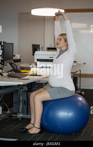 Schwangere Frau Durchführung Dehnübung auf Fitness-Ball im Büro Stockfoto
