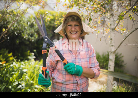 Porträt von lächelnden senior Frau hält Heckenschere stehend in Hof Stockfoto