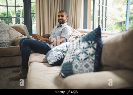 Portrait von Mann mit Laptop beim Sitzen auf der Couch zu Hause Stockfoto