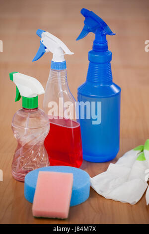 Nahaufnahme von verschiedenen Sprühflaschen, Schwamm und Handschuh auf Holzboden Stockfoto