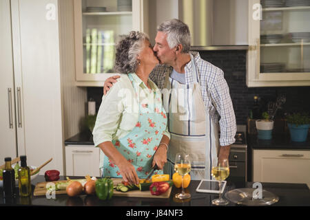 Älteres Paar küssen während der Zubereitung von Speisen in der Küche zu Hause Stockfoto