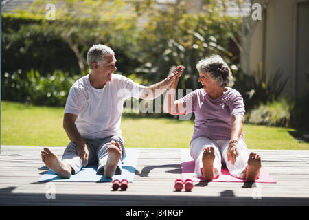 Fröhliche älteres paar geben hohe fünf während des Trainings zusammen auf Matte zu Veranda Stockfoto