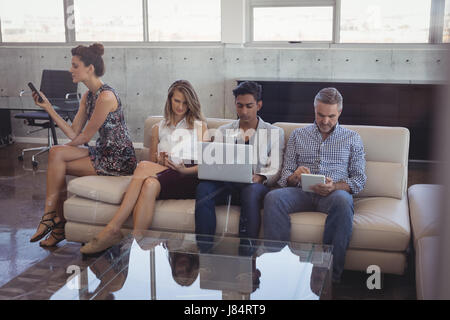 Geschäftsleute, die mit Technologien sitzend auf Sofa Kreativbüro Stockfoto