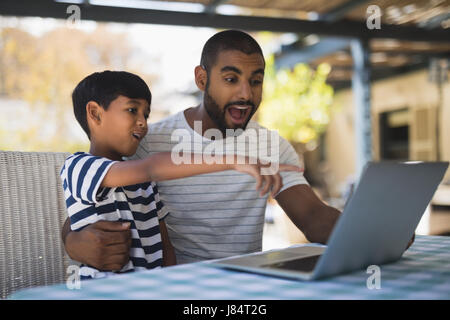 Schockiert junger Mann mit seinem Sohn betrachten Laptop auf Tisch Stockfoto