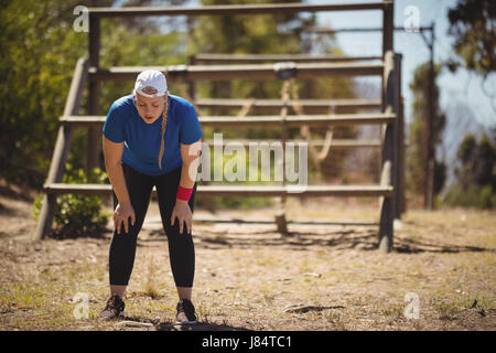 Müde Frau bücken, mit den Händen auf die Knie während der Hindernis-Parcours mit Boot camp Stockfoto