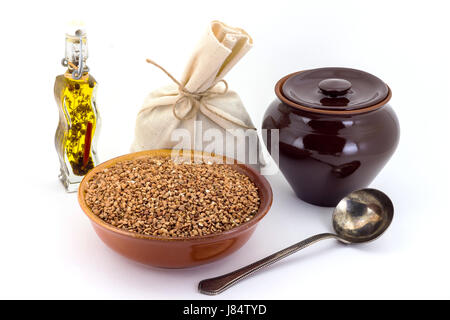 Stillleben mit Buchweizen Müsli in Keramiktopf pial, Keramik, alte Löffel und Leinentasche für Getreide, Öl, Gewürze und Würzmittel, isoliert auf weiß b Stockfoto