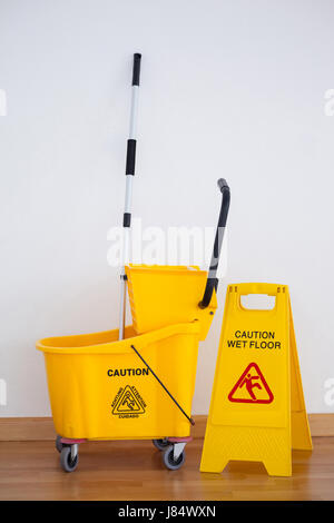 Gelbes Schild mit Mop Eimer auf Holzboden gegen Wand Stockfoto