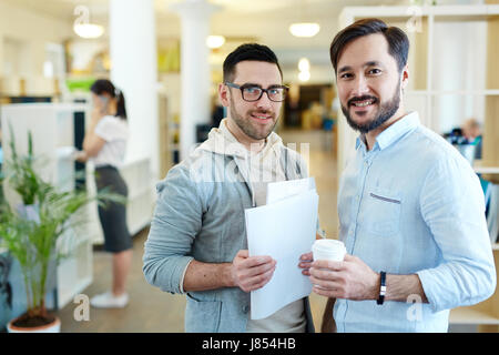 Porträt von zwei erfolgreiche Geschäftsleute gekleidet in Freizeitkleidung lächelnd Blick in die Kamera in moderne Büroflächen Stockfoto