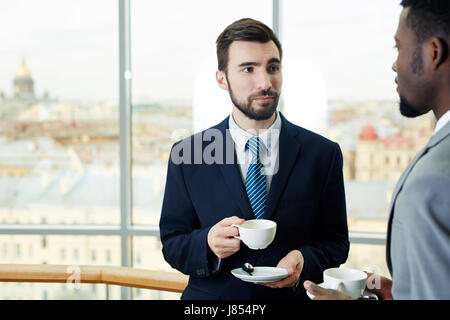 Porträt des bärtigen Jungunternehmer im Gespräch mit afrikanisch-amerikanischen Kollegen halten Tassen während der Kaffeepause Stockfoto