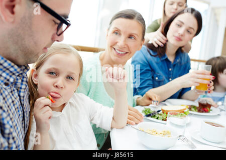 Kleines Mädchen sitzen auf den Knien des Vaters und zeigt die Zunge beim Essen frischen Erdbeere Stockfoto