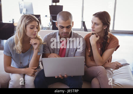 Ernsthafte junge Kollegen gemeinsam über Laptop beim Sitzen am Kreativbüro Stockfoto