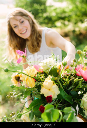 Hochzeit, Dekoration, florales Design angewandt Kunst-Konzept - im Vordergrund schöne Bouquet bestehend aus gelben Rosen, rosa Pfingstrosen und Lawinen. im Hintergrund lächelnde Frau Befestigung nur wenige Blumen Stockfoto