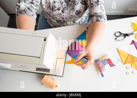 Handarbeiten und Hand Quilten in der Werkstatt von Frau Schneider auf weißem Hintergrund - hautnah an Händen mit einer Nähmaschine auf Tisch und Thread, Stoffe, Nadeln, Pins, Buttons, Schere. Stockfoto
