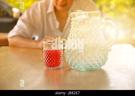 Frau sitzt und ein Glas süßen Getränk mit Glas auf Holztisch. Stockfoto