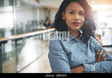 Hübsche junge verträumte afro-amerikanische Büroangestellter Stand mit verschränkten Armen und Blick in die Kamera. Stockfoto