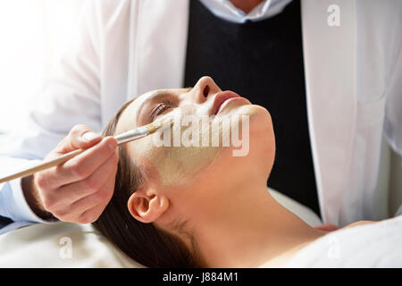 Nicht erkennbare männlichen Kosmetikerin weibliches Gesicht liegend mit geschlossenen mit Pinsel im Salon Augen Maske aufsetzen. Stockfoto