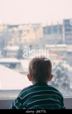 Baby Junge Blick auf den Schnee draußen vor dem Fenster Stockfoto