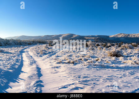 Schneebedeckte Straße führt nach gefrorenen Berg mit Winter Sonnenuntergang. Gefrorene Feld Landschaft. Stockfoto