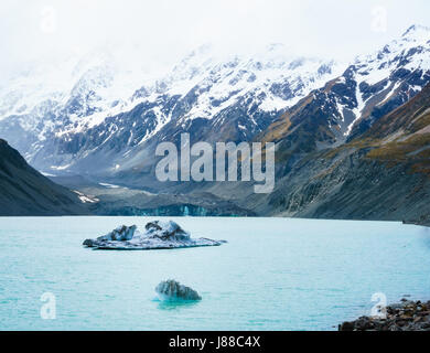 Zwei unregelmäßige Eisberge schwimmen im Hooker Lake, New Zealand. Gletscher im Hintergrund beschattet von rauen Schnee bedeckt Berge. Stockfoto