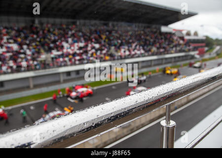 Rennwagen auf der Startaufstellung und steht voll von Fans. Der Fokus auf den Handlauf mit Regentropfen Stockfoto