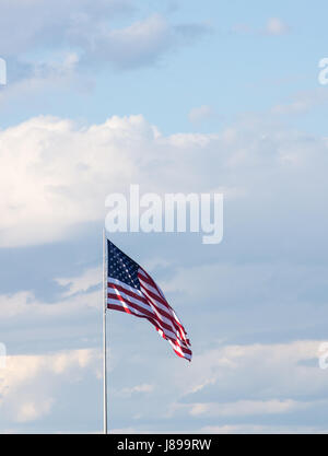 Vertikale amerikanische Flagge gegen einen hellblauen Himmel mit dünnen Wolken. Die Wolke ist im Wind entfaltet. Stockfoto