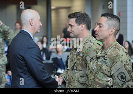 Gouverneur von Nebraska Pete Ricketts schüttelt die Hand von Nebraska Nationalgarde Chief Warrant Office 3 William Score (Pilot) nach pinning auf eine blaue und goldene Luft-Medaille mit einem Valor-Gerät. Ergebnis war eine der vier Nebraska Army National Guard Flieger ein UH-60 Blackhawk Hubschrauberbesatzung zugeordnet waren geehrt, 20 Mai, wenn sie mit der Air Medal mit "Valor" Gerät für die Tapferkeit, die sie präsentiert wurden während der Rettung von verwundeten US-Special Forces Soldaten am 9. Februar 2017, in der Nähe von Sangin, Afghanistan in der Provinz Helmund angezeigt. Die vier Nebraska Army National Guard Soldaten sind Mitglieder des Gua Stockfoto