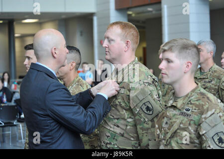 Gouverneur von Nebraska Pete Ricketts pins auf eine blaue und goldene Luft-Medaille mit einer Tapferkeit Staff Sgt Matthew Hawke (Helicopter Crew Chief). Hawke war einer der vier Nebraska Army National Guard Flieger ein UH-60 Blackhawk Hubschrauberbesatzung zugeordnet waren geehrt, 20 Mai, wenn sie mit der Air Medal mit "Valor" Gerät für die Tapferkeit, die sie präsentiert wurden während der Rettung von verwundeten US-Special Forces Soldaten am 9. Februar 2017, in der Nähe von Sangin, Afghanistan in der Provinz Helmund angezeigt. Die vier Nebraska Army National Guard Soldaten sind Mitglieder der Garde Lincoln ansässige Unternehmen G, 2-104 General Stockfoto