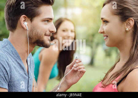 Happy Teens Entspannung im Park, ein Kerl teilt seine Kopfhörer mit einem Mädchen, sie sind gegenseitig anstarren Stockfoto