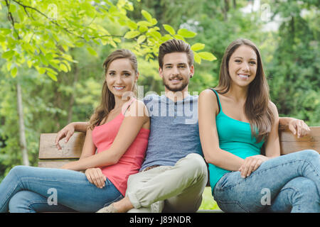 Lächeln Jugendliche entspannen im Park an einem Sommertag, sie sitzen auf einer Holzbank und Blick in die Kamera Stockfoto