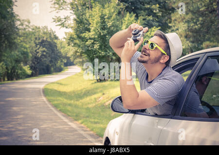 Porträt des jungen begeistert Touristen Kerl die Fotos vom Fahrersitz auf Straße Reise Reisen Urlaub. Aufnahme aus Fenster mit Vintage retro-c Stockfoto