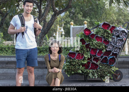 Porträt-Paare der jüngeren asiatischen Reisen, Mann und Frau sitzen am Straßenrand neben roten Rosen Blumenstrauß Stockfoto