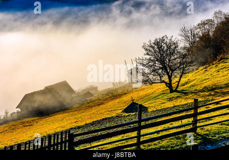 ländliches Gebiet am Hang im Herbst. landwirtschaftlichen Bereich und Häuser im Nebel hinter dem Zaun. schönen und lebendigen Landschaft Landschaft. Stockfoto