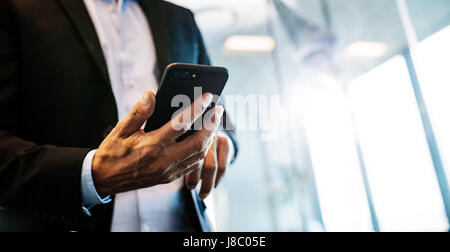 Bild des männlichen Unternehmer mit Handy im Büro beschnitten. Konzentrieren Sie sich auf Händen der Geschäftsmann mit Ihrem Smartphone. Stockfoto