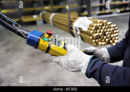 Nahaufnahme des Arbeitnehmers Hände in Handschuhe indoor Brückenkran auf Fabrik drücken Tasten auf Anhänger, Metall zu erheben, die Rohre in fließend zu manipulieren Stockfoto
