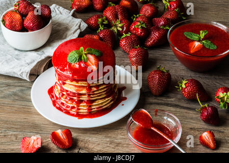 Amerikanische Pfannkuchen und Erdbeersauce und Darm mit einer Beere auf einem hölzernen Hintergrund. Große Schärfentiefe. Stockfoto