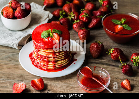 Amerikanische Pfannkuchen und Erdbeersauce und Darm mit einer Beere auf einem hölzernen Hintergrund. Geringe Schärfentiefe. Stockfoto